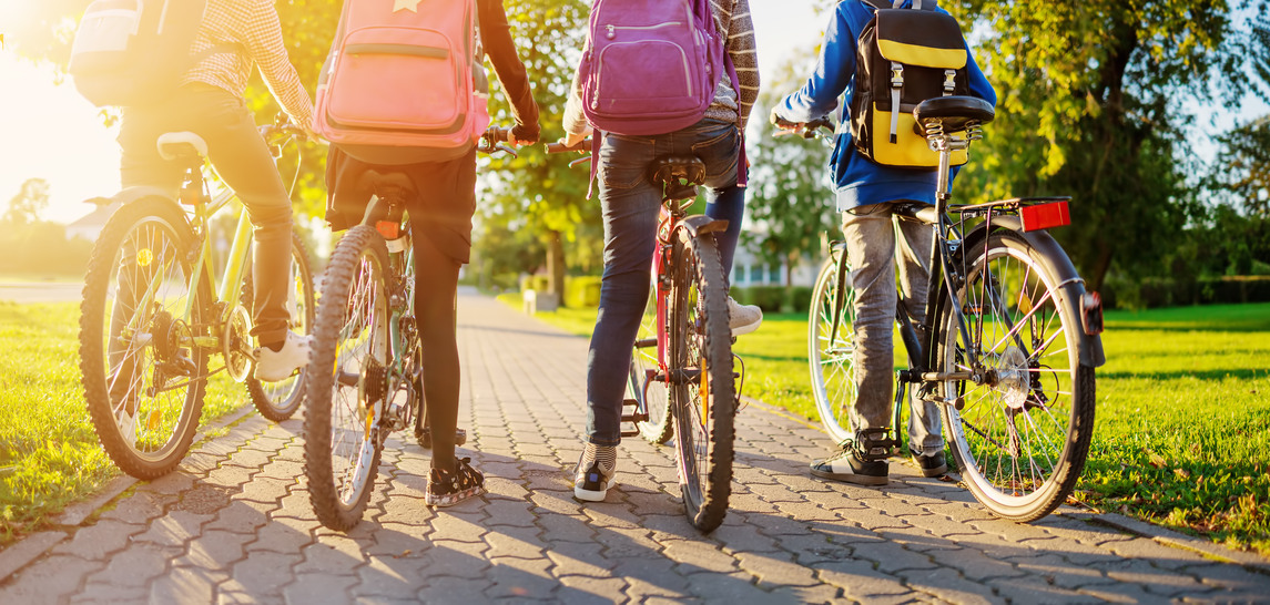 Fyra barn med cyklar och ryggsäckar på en solig cykelbana